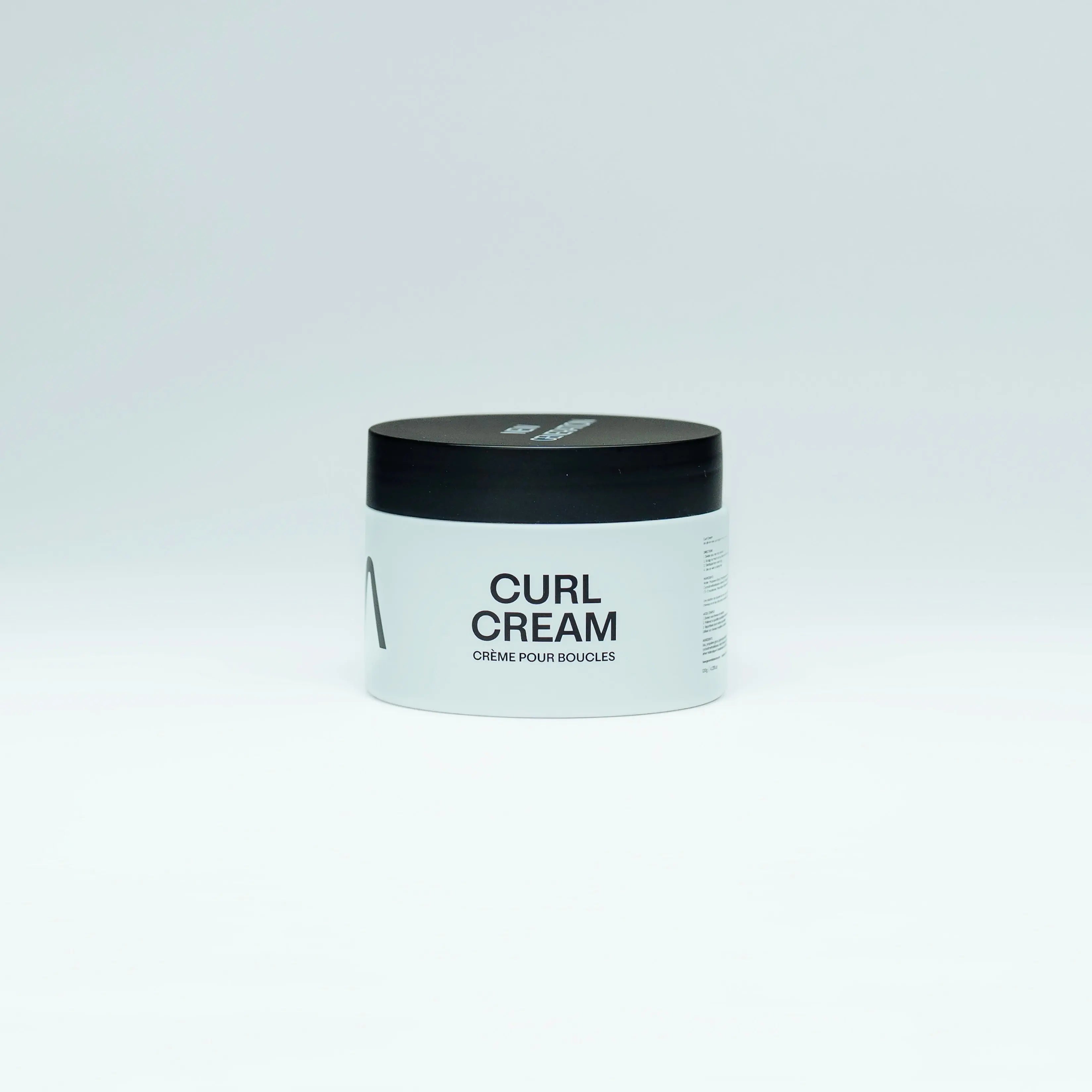 Jar of aura curl cream with black lid and white body on a light gray background